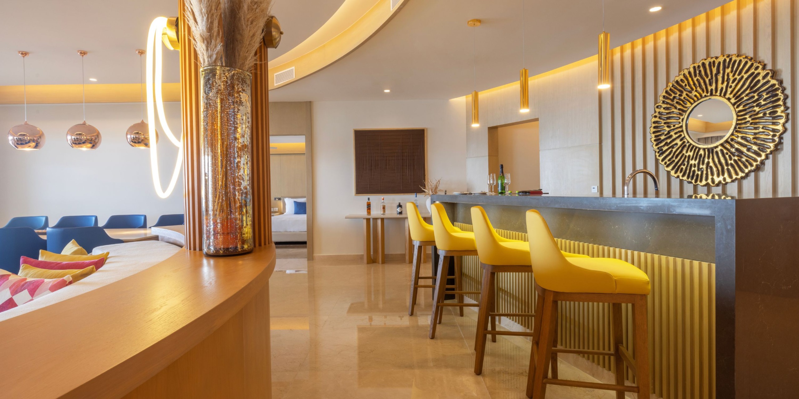 Modern bar area at Royalton Splash Riviera Cancun featuring yellow barstools, a decorative circular mirror, and ambient lighting.