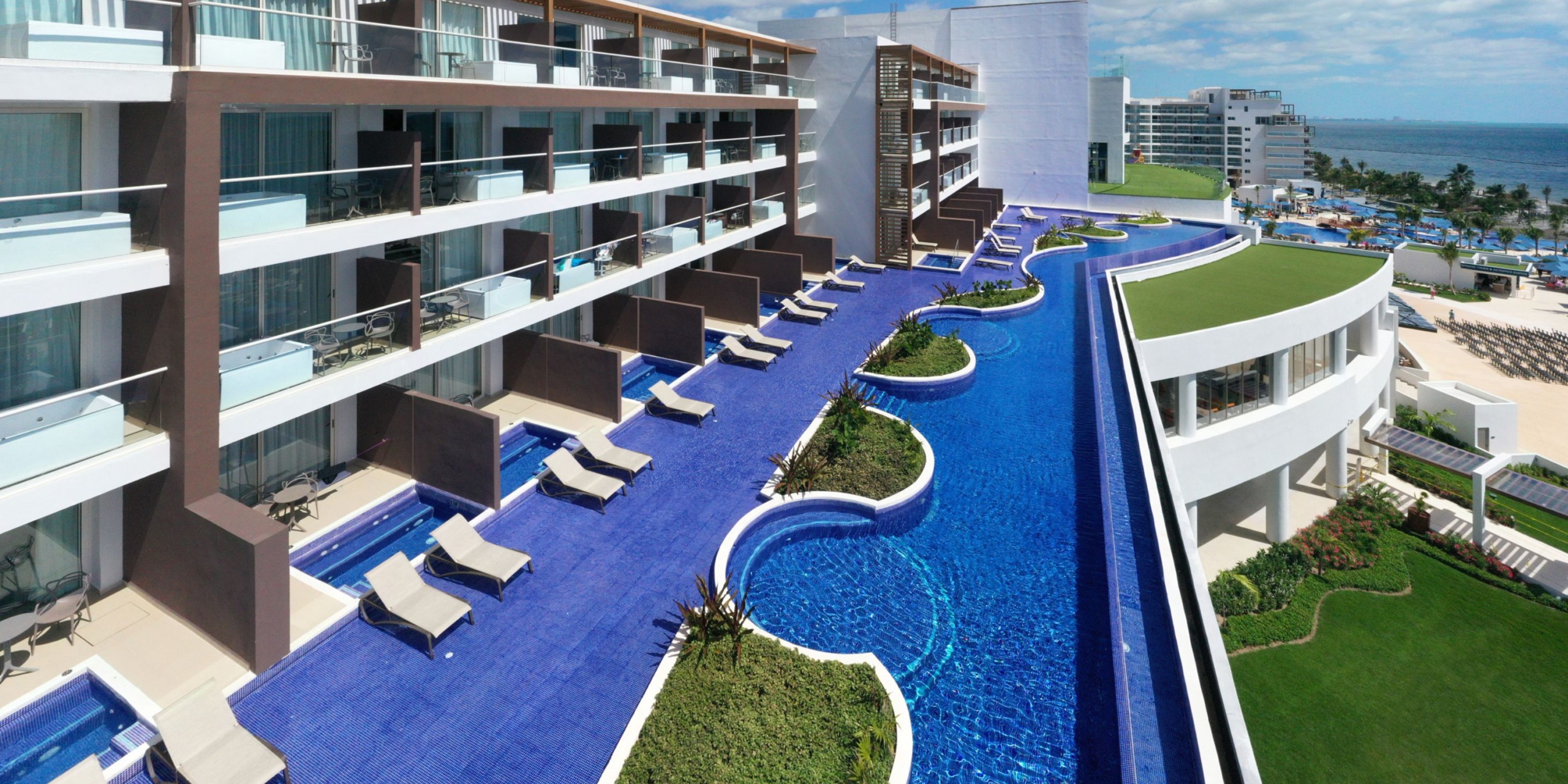 The Royalton Splash Riviera Cancun is a contemporary hotel featuring a collection of private pools on individual balconies, each offering views of a central large pool and the ocean in the background.