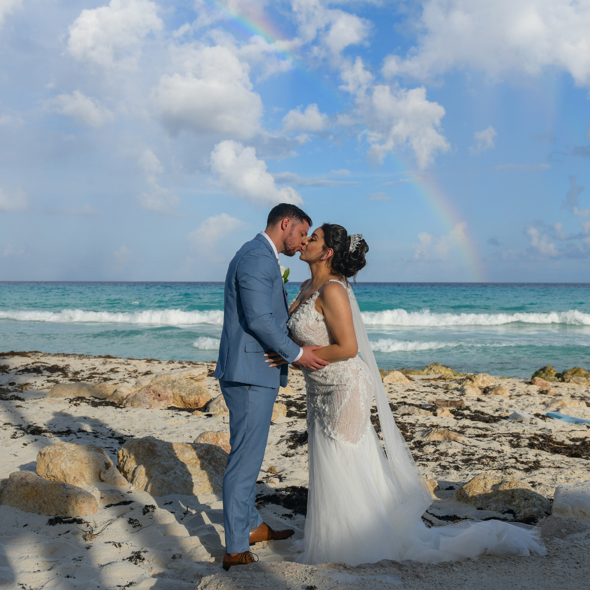 Gorgeous couple kissing on one of the best Mexico Wedding Venues with a rainbow in the distance