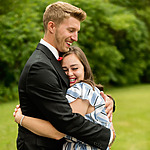 A smiling man in a black suit embraces a happy woman in a striped dress at their Destify wedding outdoors.