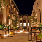 Courtyard dining area ideal for destination weddings, featuring string lights, lush greenery, and modern furniture against a backdrop of a multi-story building with lit windows.