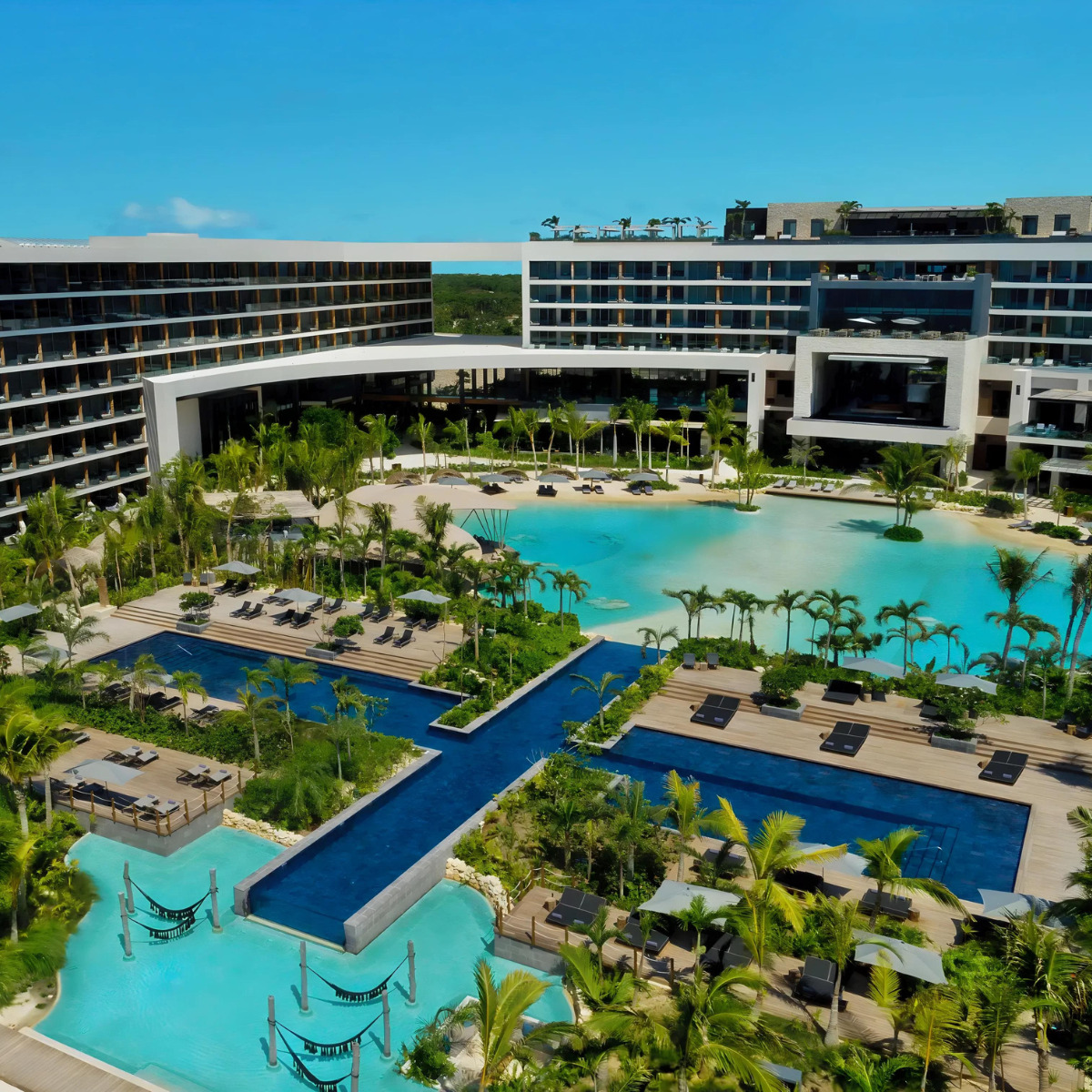 Aerial view of Secrets Impression Moxché Playa del Carmen, a sought-after destination for weddings, featuring a large swimming pool surrounded by palm trees and modern buildings.