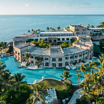 Aerial view of a luxurious coastal resort ideal for a destify wedding, with a large swimming pool and palm trees, surrounded by the sea.