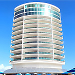 Modern cylindrical building with glass facade under a clear blue sky at Playa Resorts.