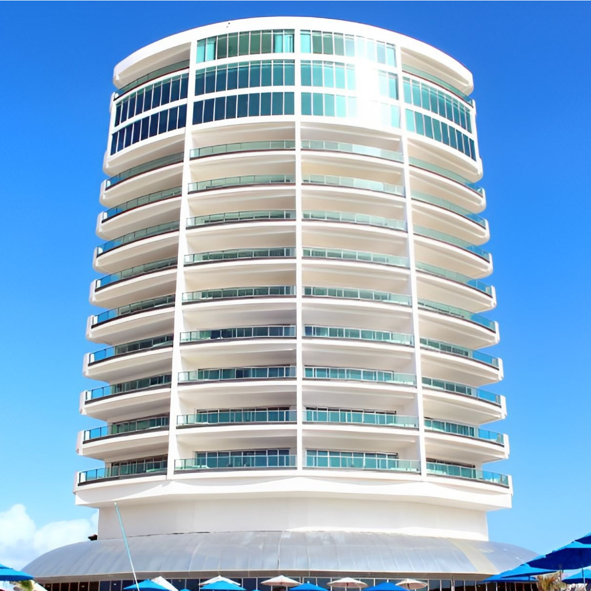 Modern cylindrical building with glass facade under a clear blue sky at Playa Resorts.