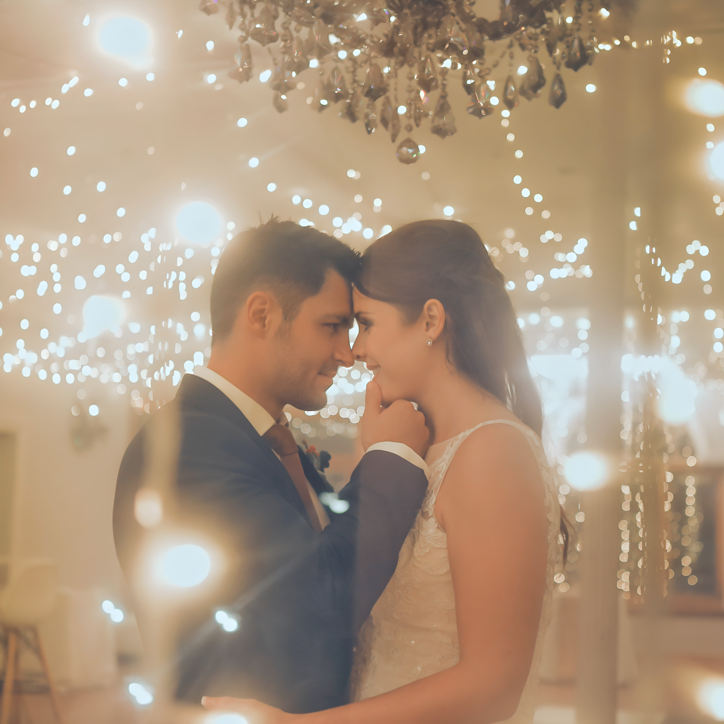 A newlywed couple intimately gazing into each other's eyes under a canopy of twinkling lights at their destination wedding.