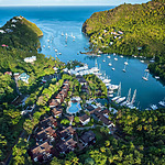 Aerial view of Zoetry Marigot Bay, a lush tropical marina with boats moored in clear blue waters, surrounded by dense greenery and luxury resort facilities.