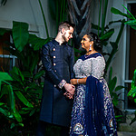 A couple in traditional Indian attire smiling and holding hands in a lush Caribbean garden.