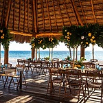 A destination wedding reception set up on the beach with tables and chairs, offering various wedding packages prices.