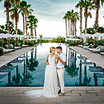A bride and groom posing in front of a pool with palm trees for their destination wedding.