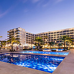 Dreams Karibana Cartagena Golf & Spa Resort ideal for destination weddings, featuring a large, illuminated outdoor swimming pool at twilight, surrounded by palm trees and a multi-story building.