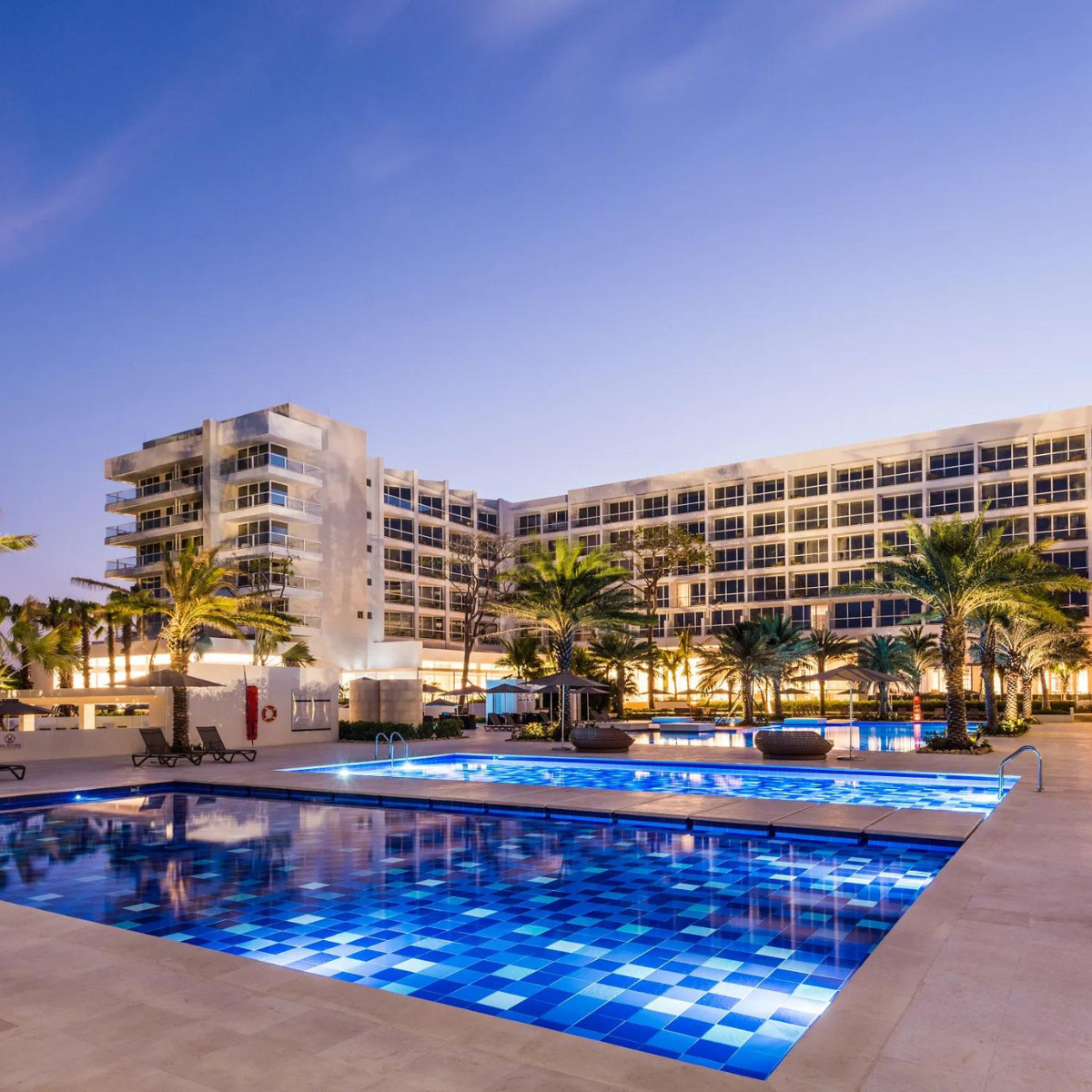 Dreams Karibana Cartagena Golf & Spa Resort ideal for destination weddings, featuring a large, illuminated outdoor swimming pool at twilight, surrounded by palm trees and a multi-story building.