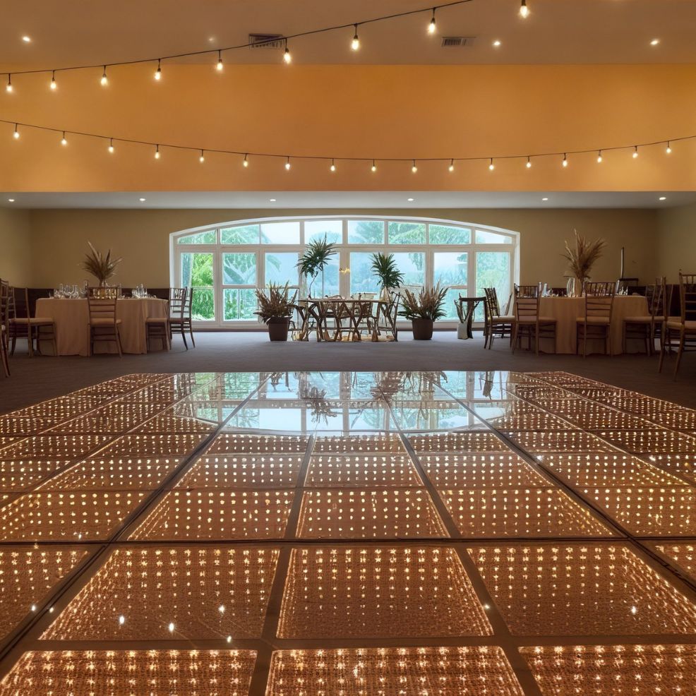 A beautifully illuminated dance floor gracing an empty banquet hall, adorned with string lights and large windows, sets the perfect scene for a dreamy destination wedding.