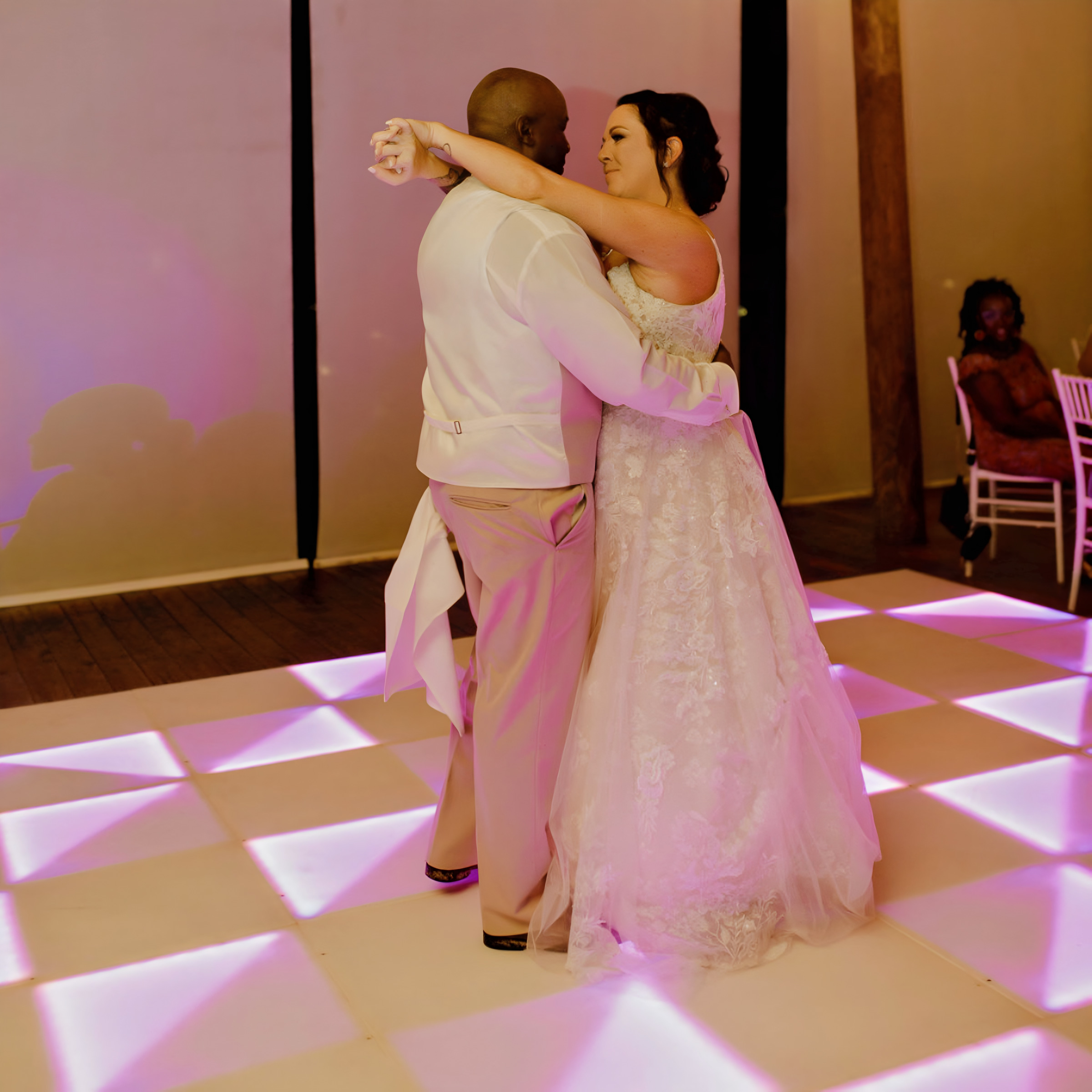 A bride and groom share a dance on a light-up dance floor at their destination wedding reception, looking into each other's eyes.