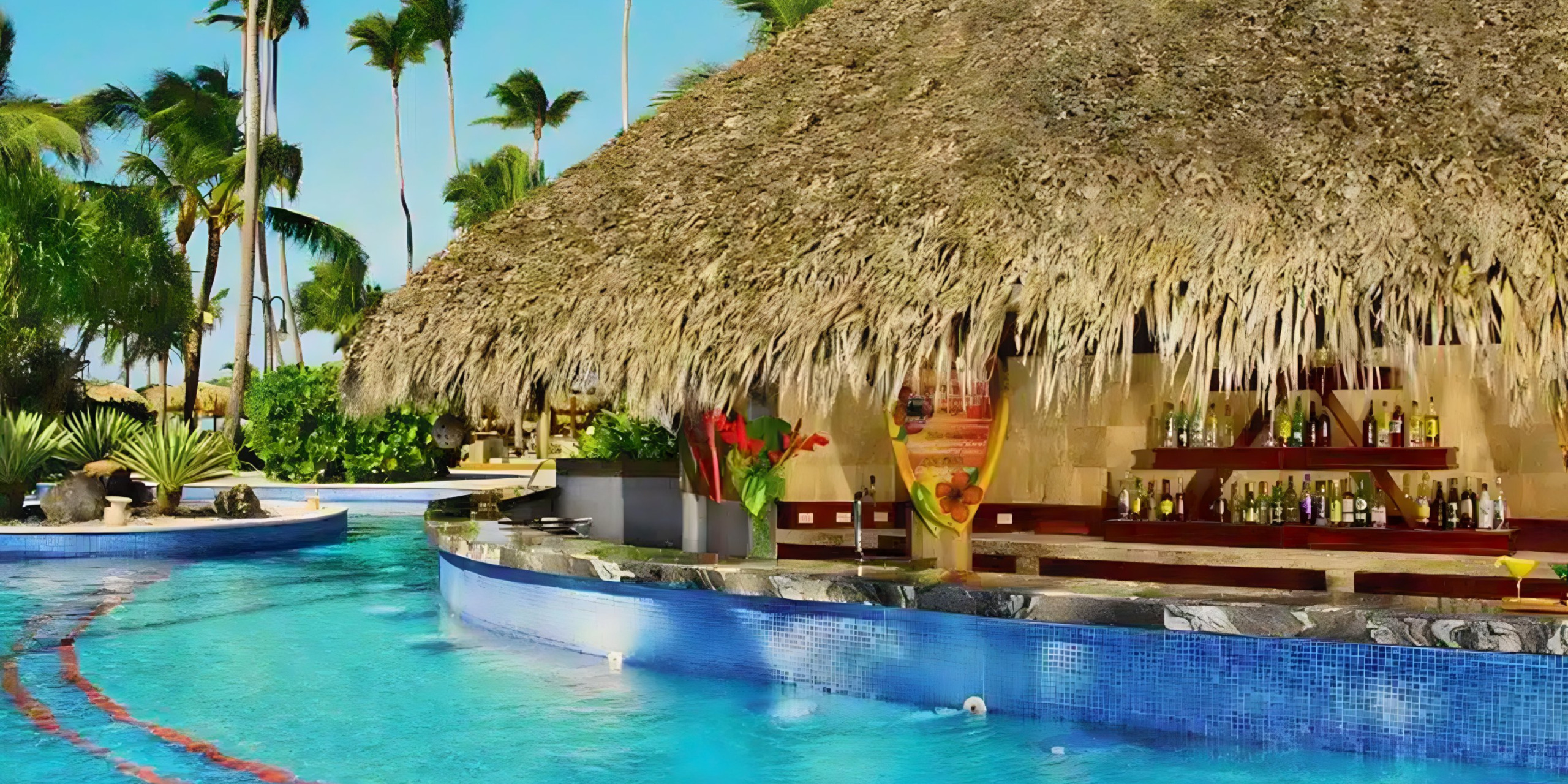 A swim-up bar with a thatched roof next to a vibrant blue pool surrounded by palm trees at Jewel Punta Cana, perfect for destination weddings.