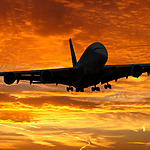 A commercial airplane silhouetted against a vibrant orange sunset sky, descending for landing with extended landing gear, carrying guests to a destination wedding.