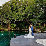 A bride and groom share a kiss on a wooden dock by a serene natural pond surrounded by lush greenery, perfect for destination weddings.