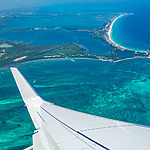 Aerial view from an airplane showing the wing over vibrant turquoise ocean waters near a coastal city, a popular destination wedding locale.