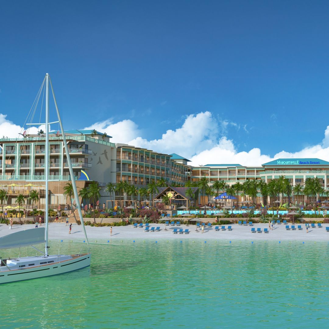 A tropical resort destination for weddings, featuring a large hotel building, palm trees, a sandy beach with loungers, and a sailboat on clear turquoise water under a blue sky.