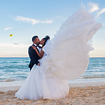 A Aushiree and Robert in wedding attire embracing on a destination wedding beach with the bride's dress trailing in the wind.