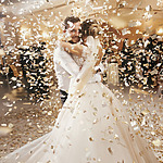 A bride and groom embrace joyfully at their destination wedding while surrounded by a shower of golden confetti.