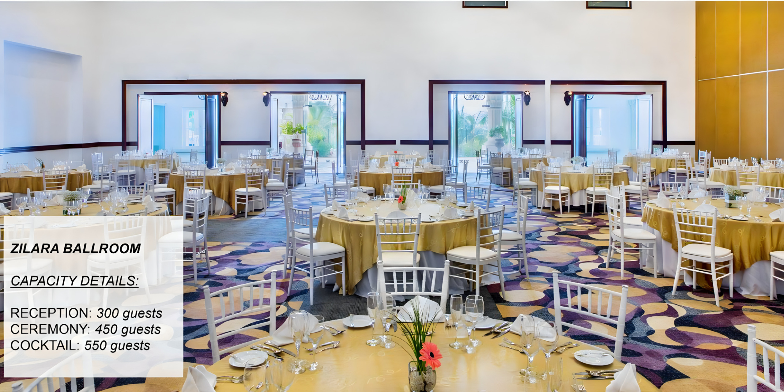 A spacious ballroom set with round tables draped in gold tablecloths, with chairs and red floral centerpieces, designed for large events such as a destination wedding.