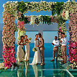 A bride and groom standing under a glass wedding arch during their wedding ceremony.
