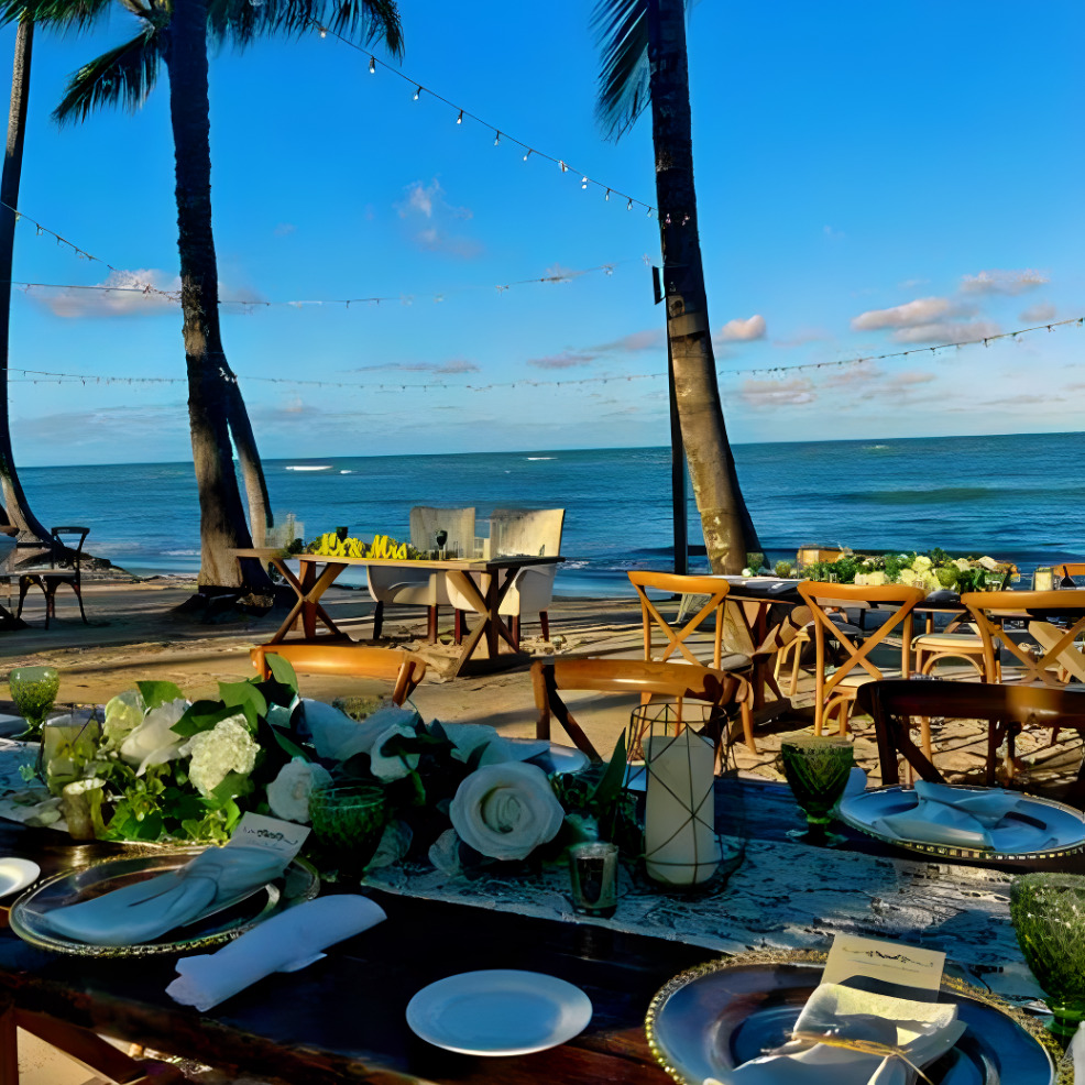 A destination wedding table set up on the beach with palm trees in the background.