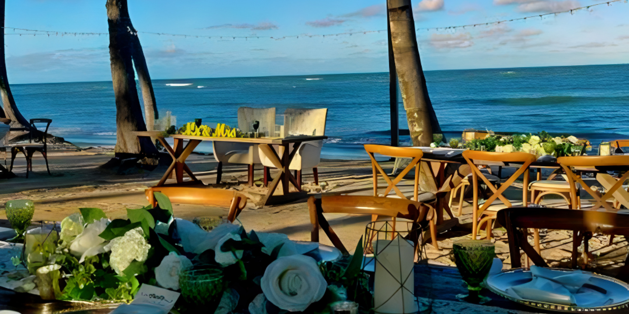 A destination wedding table set up on the beach with palm trees in the background.