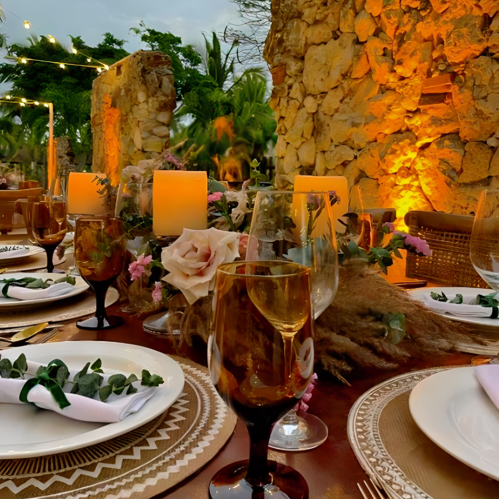 A destination wedding table setting with candles and flowers on a stone wall.