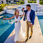 A bride and groom standing next to a pool at their wedding.