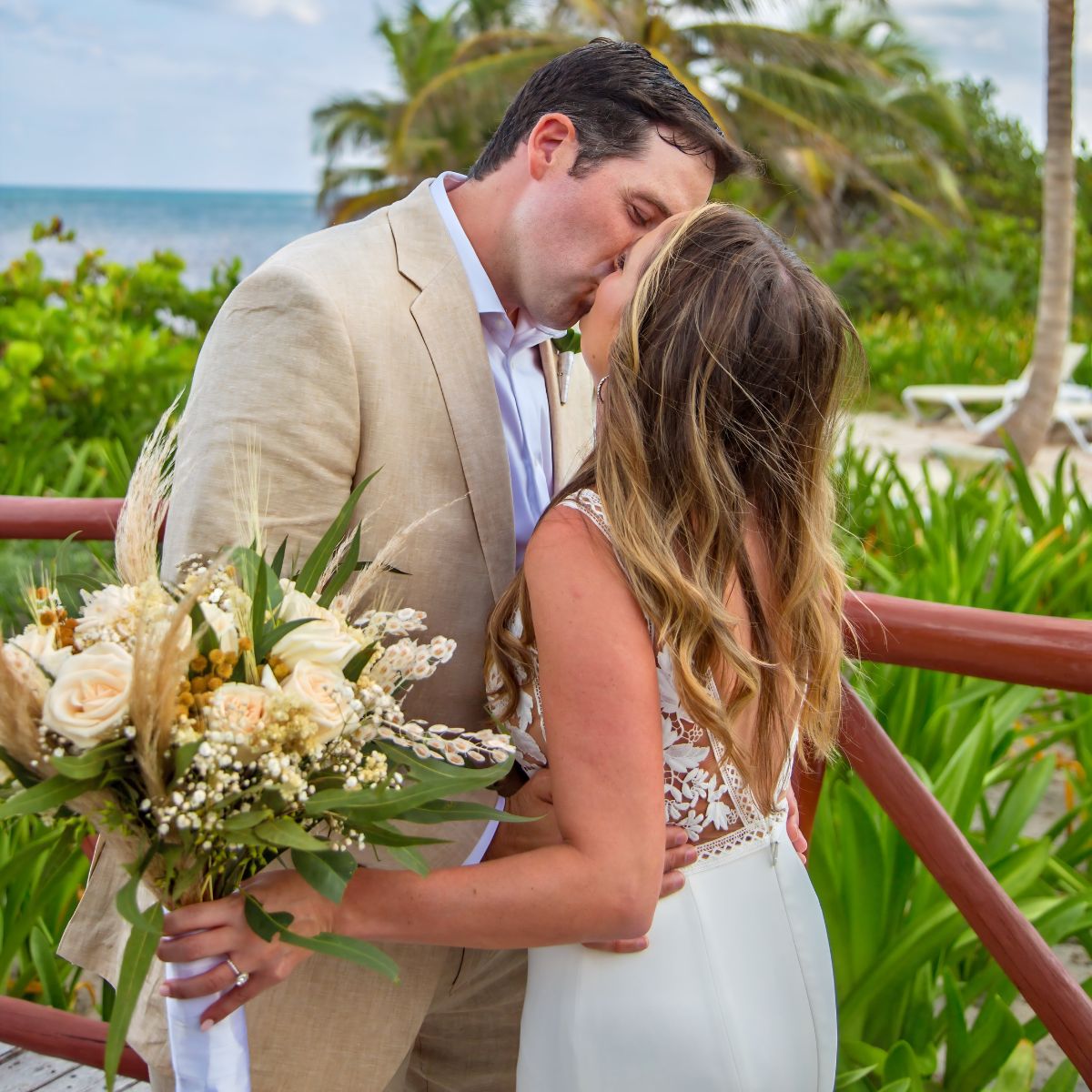 A bride and groom share a wedding kiss in front of the ocean.
