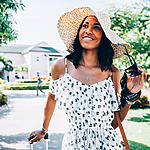 A woman heading to a destination wedding, wearing a straw hat and a dress, holding a suitcase.