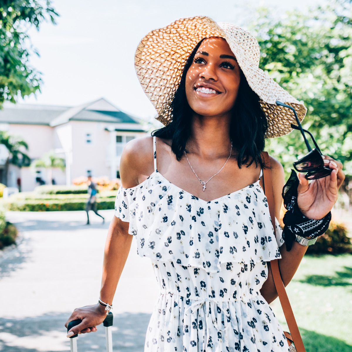 A woman heading to a destination wedding, wearing a straw hat and a dress, holding a suitcase.