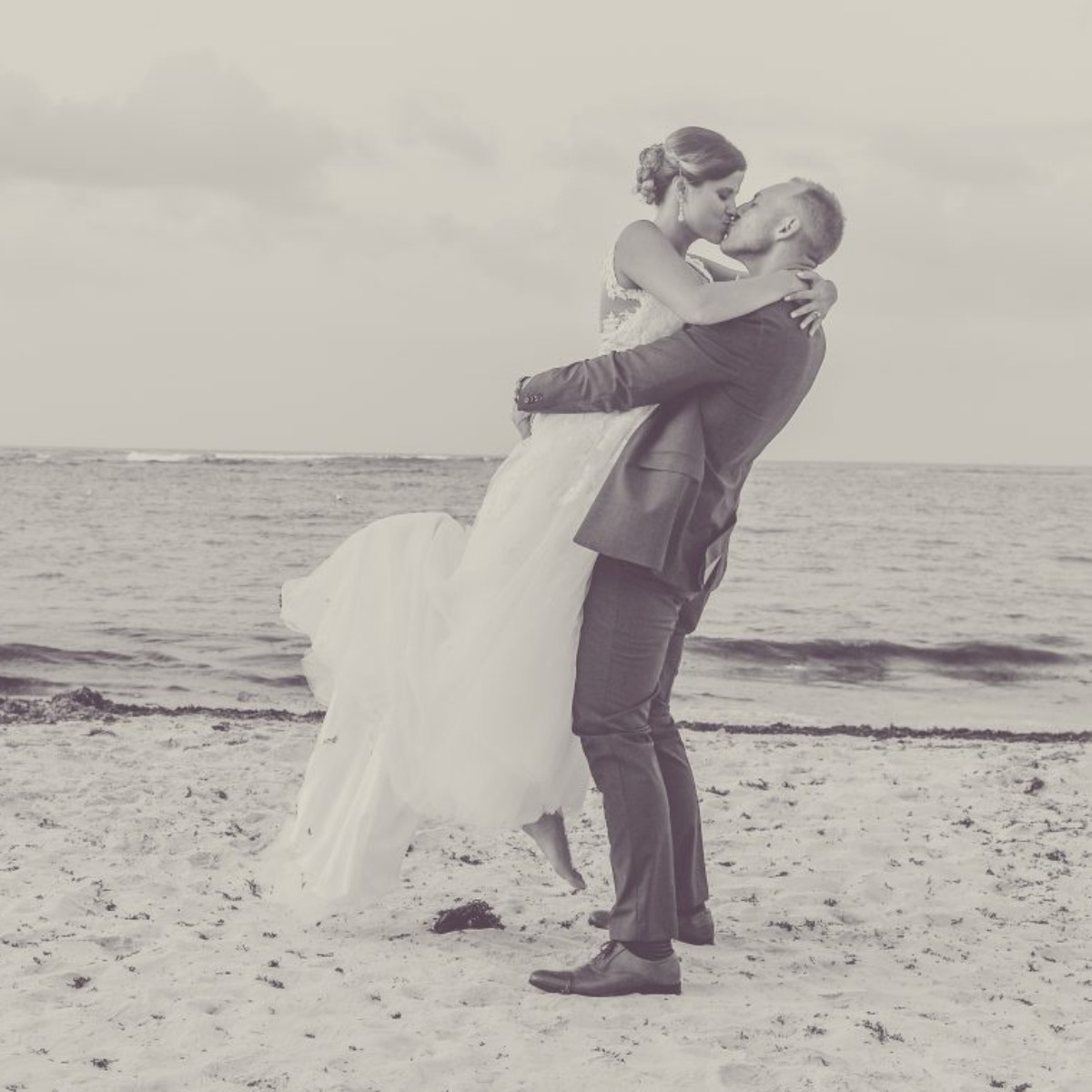 A bride and groom embracing on the sandy beach.