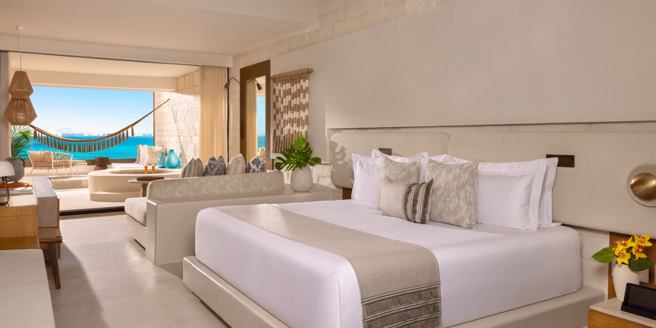 Experience luxury at its finest in a room at Impression Isla Mujeres by Secrets, featuring a king-size bed, modern decor, and a balcony with seating and a hammock that offers stunning ocean views.
