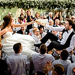 A bride and groom are being carried by a group of people at their wedding.