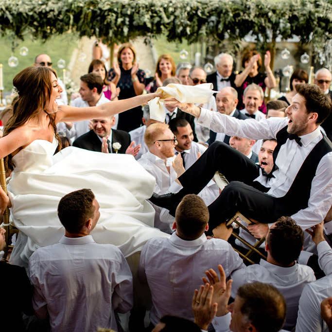 A bride and groom are being carried by a group of people at their wedding.