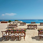 A wedding ceremony set up on the beach with chairs and flowers.