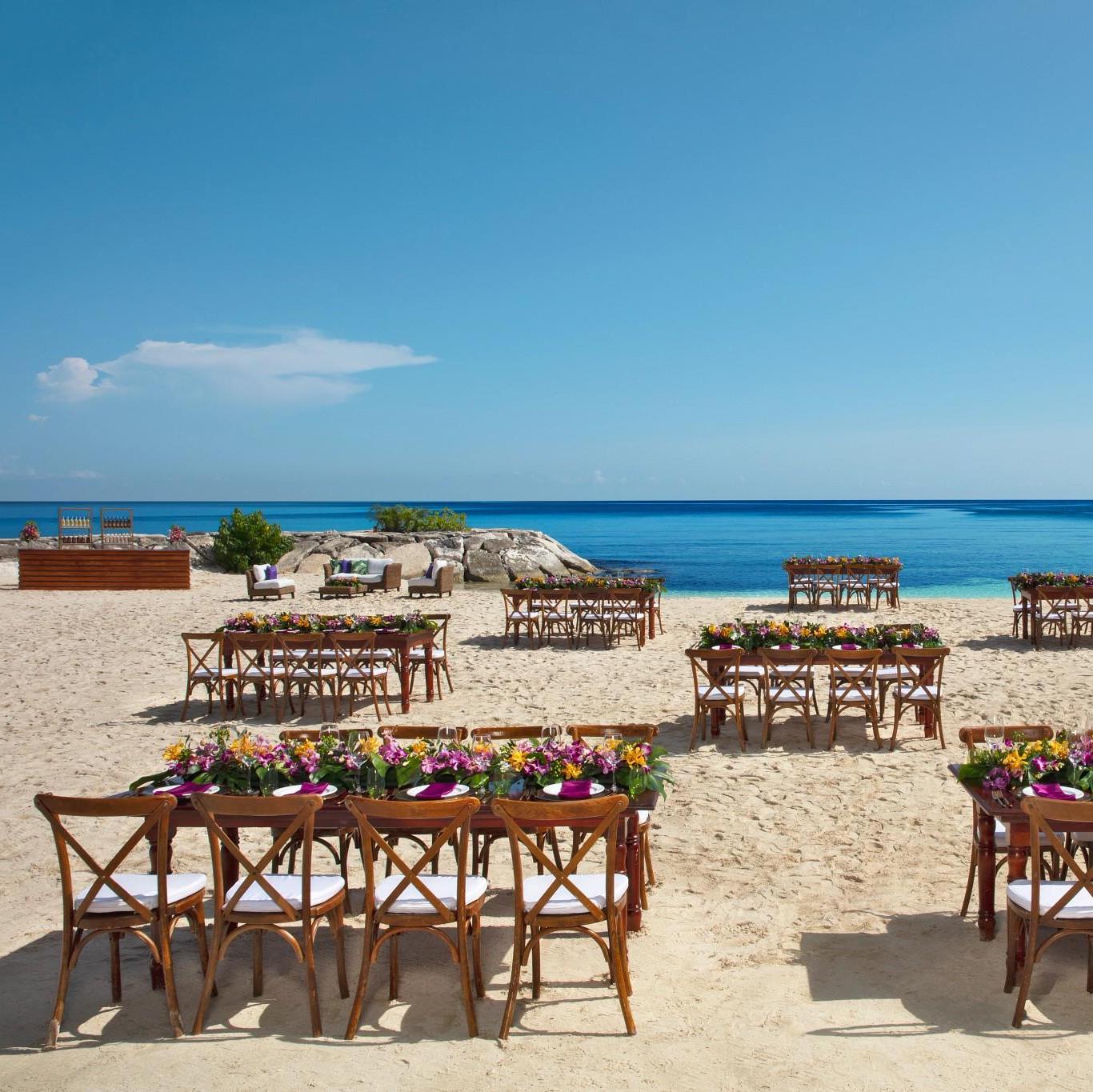 A wedding ceremony set up on the beach with chairs and flowers.