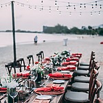 A wedding table set up on the beach with destify red and white place settings.