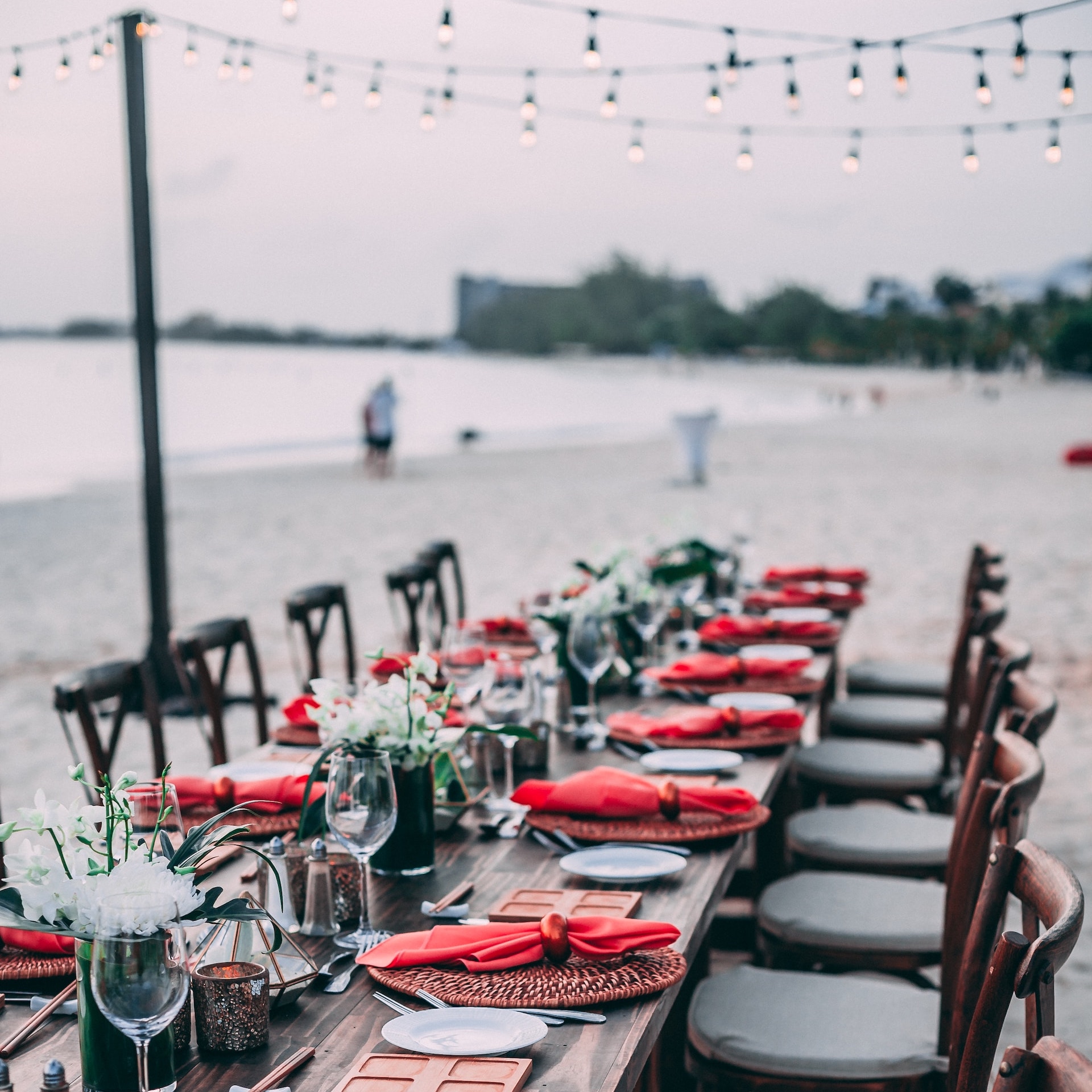 A wedding table set up on the beach with destify red and white place settings.