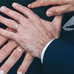 A group of men's hands holding each other's wedding rings at a same-sex wedding.