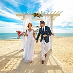 A bride and groom walking down the aisle on the beach to celebrate their 30th wedding anniversary.