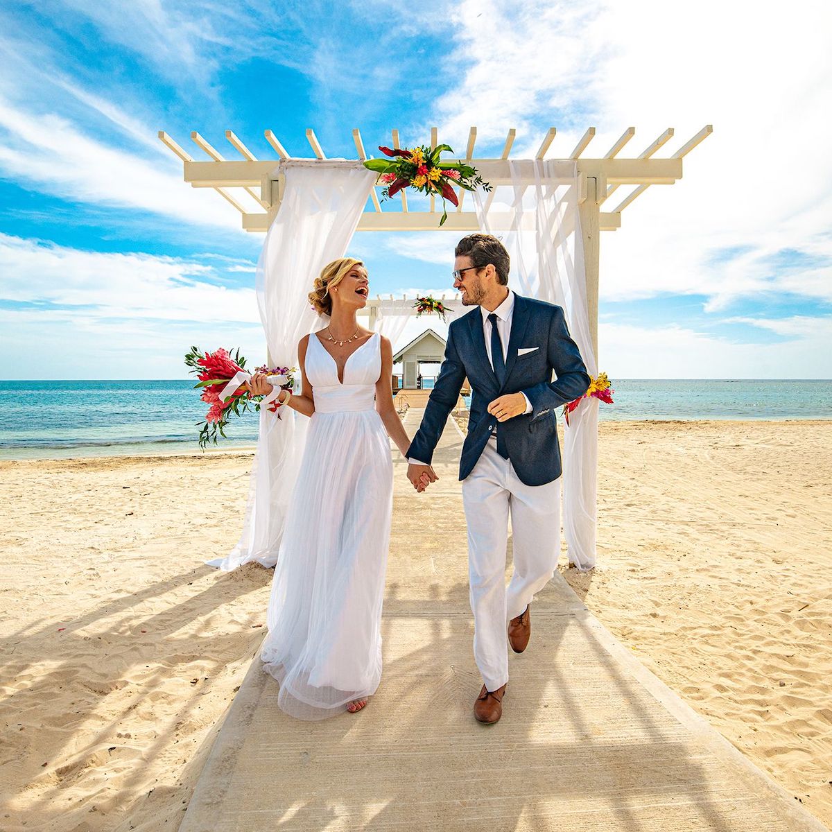 A bride and groom walking down the aisle on the beach to celebrate their 30th wedding anniversary.