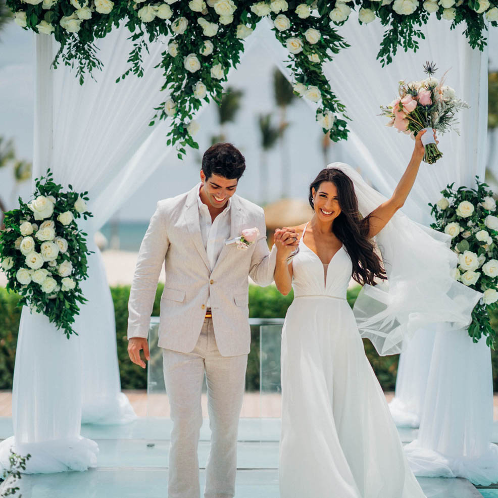 A bride and groom walk down the aisle at their wedding in cancun.