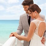 Bride and groom stand by a railing at their destination wedding, highlighting the seaside celebration.