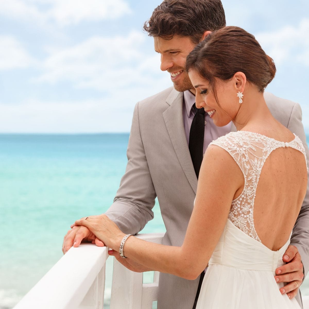 Bride and groom stand by a railing at their destination wedding, highlighting the seaside celebration.