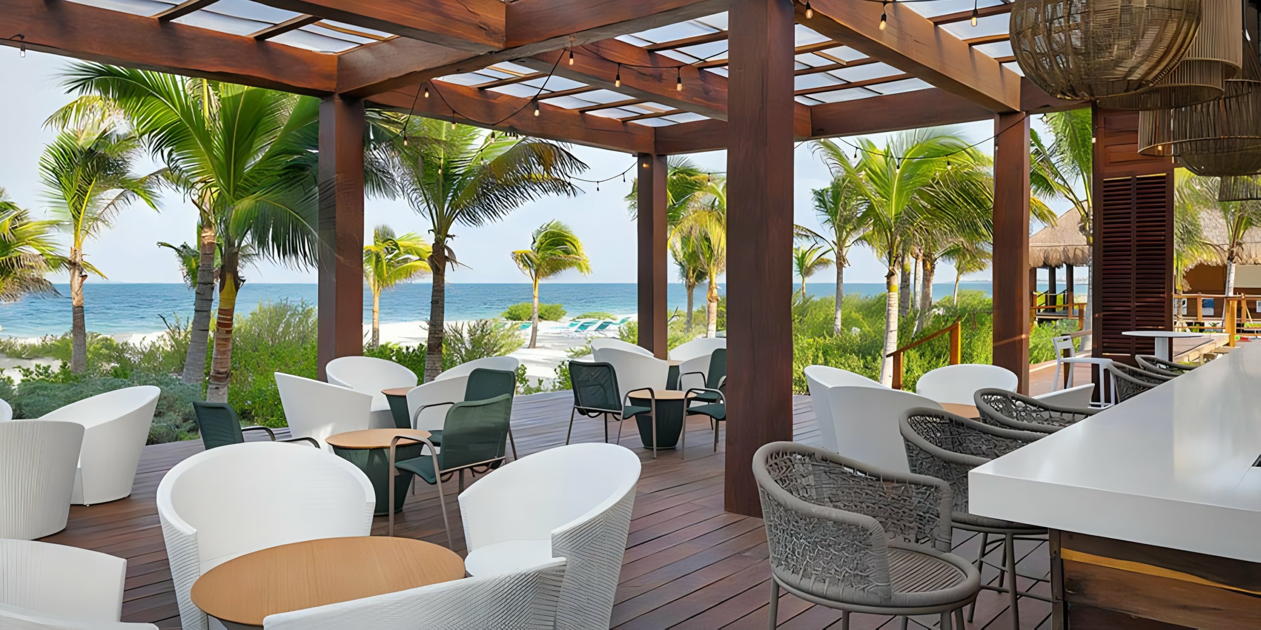 An outdoor bar with white chairs and a view of the ocean at Catalonia Grand Costa Mujeres.