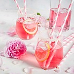 Two glasses of pink lemonade, a signature cocktail idea, surrounded by roses.